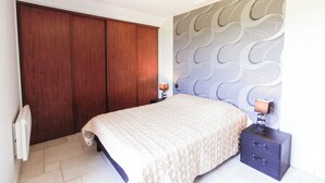 A bedroom with a bed, a nightstand, a lamp, a wardrobe, and a wall with a wavy pattern. - Entre Plages & Espagne : Ferme de Charme, Pistes cyclables & Baignade Bio (Orx)