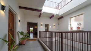 A corridor with potted plants, a wooden door, and a balcony with a railing. - The Munshi Mansion (Jodhpur)