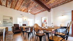 A rustic dining area with exposed wooden beams, a wooden table set for four, and a variety of chairs. - The Munshi Mansion (Jodhpur)