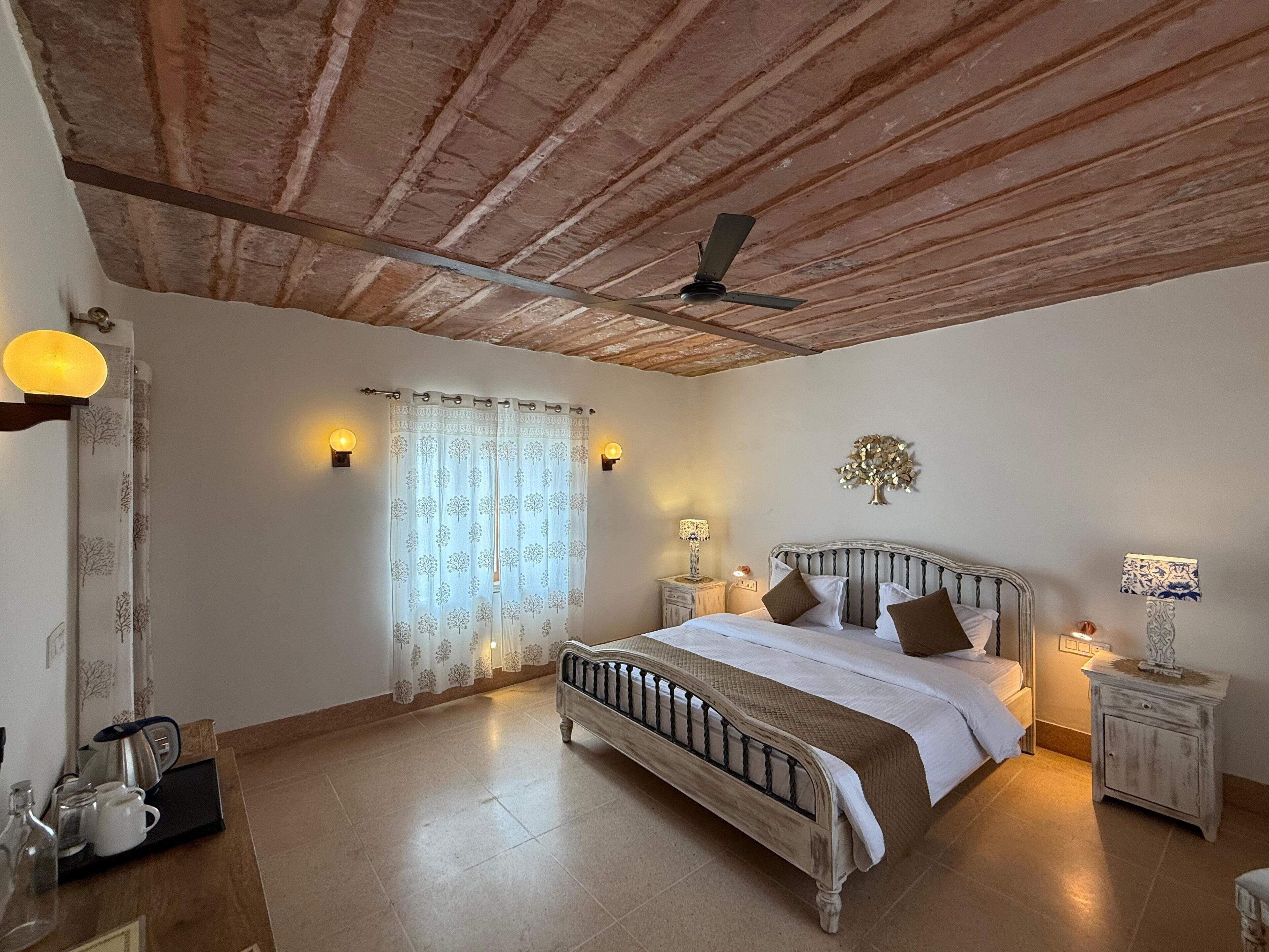 Une chambre avec un plafond en bois, un lit avec une tête de lit, deux tables de chevet avec des lampes et une fenêtre avec des rideaux.