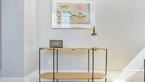 A minimalist room with a wooden console table, a framed picture on the wall, and a small table lamp. - Steps to Bourbon Street | Superior 2BDR Suite (New Orleans)