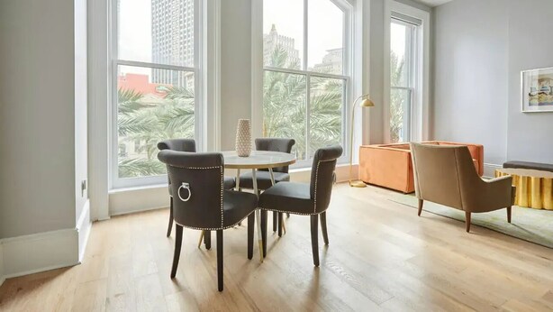 Ein geräumiges Zimmer mit großen Fenstern, einem runden Esstisch mit Stühlen und einem Sofa.