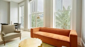 Ein modernes Wohnzimmer mit einem beigen Sofa, einem runden Couchtisch und Blick auf Palmen durch große Fenster.