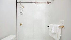 Ein modernes Badezimmer mit einer gläsernen Dusche, weißen Fliesen und einer weißen Badewanne.