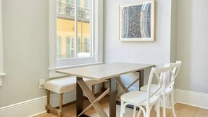Ein Essbereich mit Tisch und Stühlen, ein Fenster mit Blick auf Gebäude und ein gerahmtes Bild an der Wand.