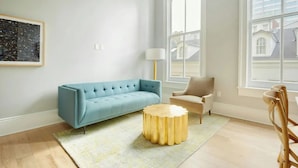 A modern living room with a blue sofa, a round gold side table, and a beige armchair. - Steps to Bourbon Street | Hearing-Accessible 2BDR (New Orleans)