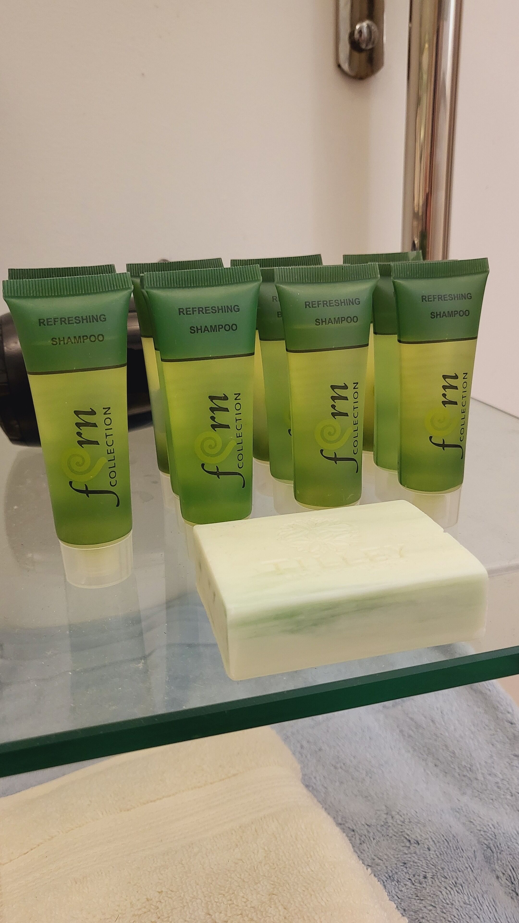 Uma fileira de frascos verdes de shampoo com a etiqueta 'femin Collection' em uma prateleira de vidro.
