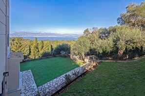 A backyard with a stone pathway leading to a green lawn, surrounded by trees and a view of a lake and mountains.