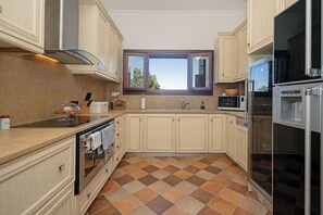 A kitchen with a tiled floor, a window, and modern appliances including a refrigerator and microwave.