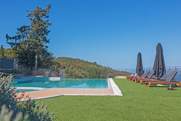 A swimming pool with a clear blue sky, surrounded by grass and trees.