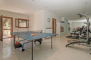 A spacious room with a ping pong table, exercise equipment, and large windows.