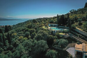 A secluded villa with a swimming pool surrounded by lush greenery and a view of the sea.