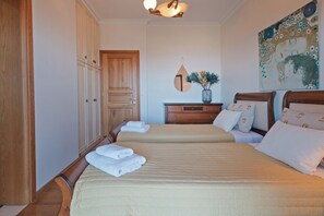 A hotel room with two beds, wooden wardrobe, a mirror, a vase with flowers, and a painting on the wall.