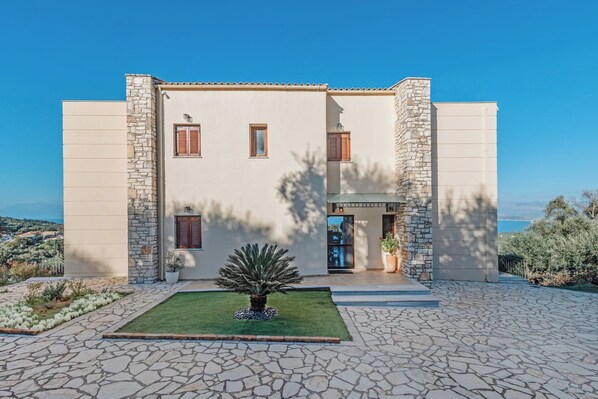 A two-story building with stone and plaster exterior walls, a small front garden, and a paved driveway.