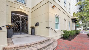 A building with a large garage door, steps leading to a door, and a brick pathway. - Modern 2BDR ADA in Walkable Historic District | The Juliette #102 by AvantStay (Savannah)