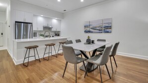 A modern kitchen with white cabinets, a stainless steel refrigerator, and a dining area with a white table and grey chairs. - Modern 2BDR ADA in Walkable Historic District | The Juliette #102 by AvantStay (Savannah)