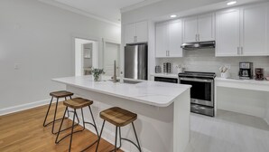 A modern kitchen with white cabinetry, a stainless steel refrigerator, an oven, and a built-in stove. There are three wooden stools at the island. - Modern 2BDR ADA in Walkable Historic District | The Juliette #102 by AvantStay (Savannah)
