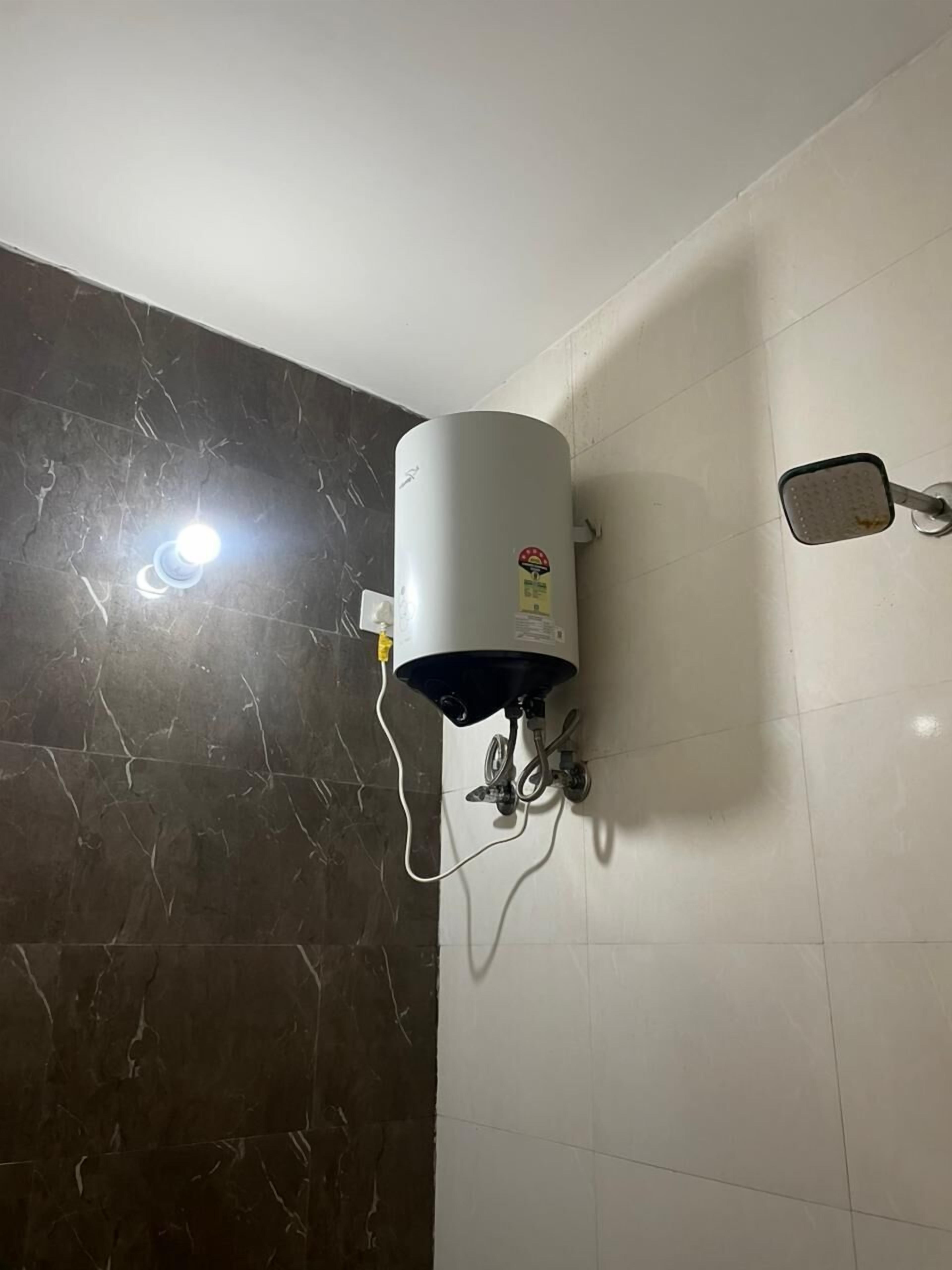 A bathroom with a water heater mounted on the wall, a hand dryer, and a mirror.