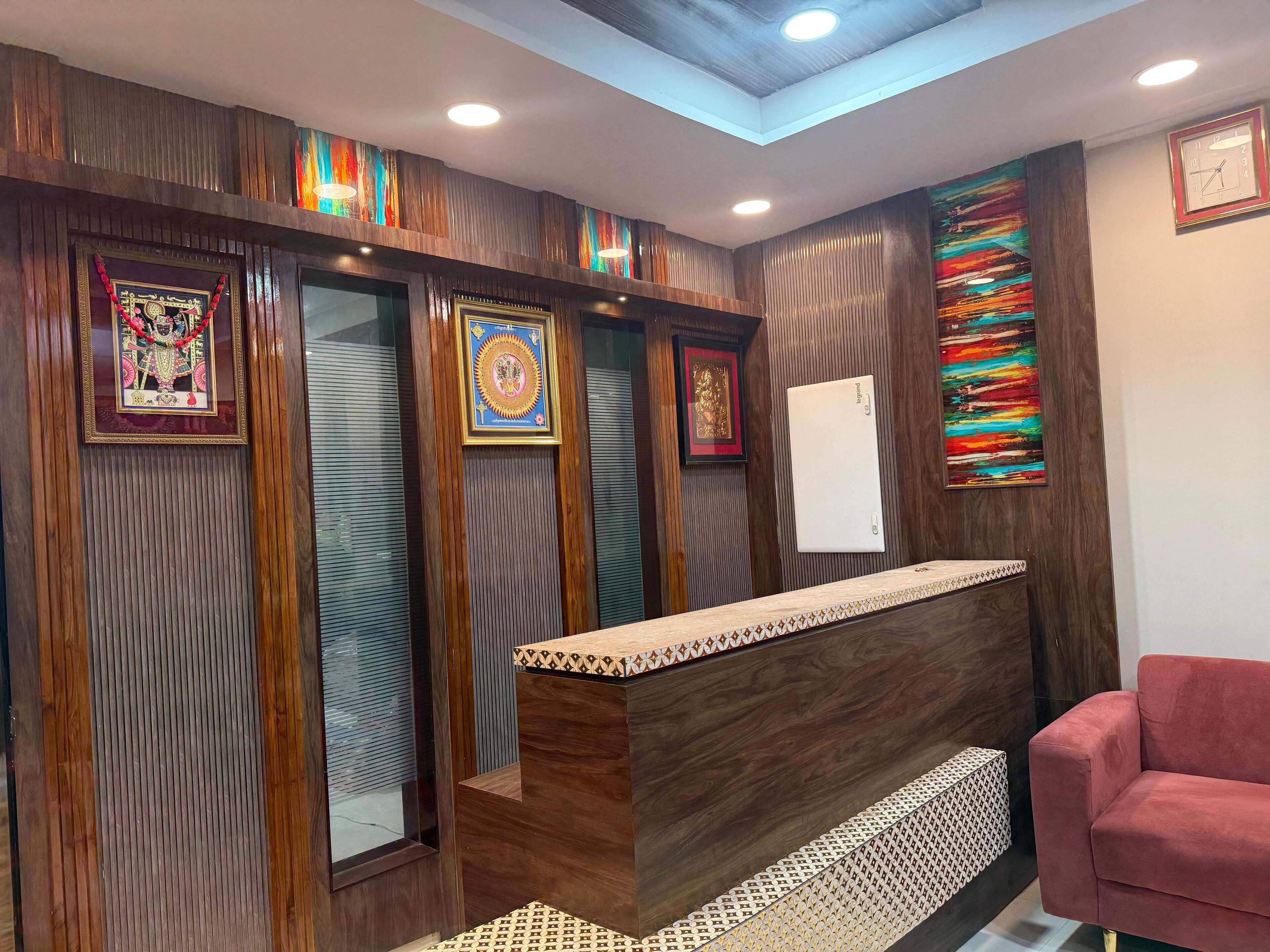 A reception area with a wooden reception desk, framed religious artifacts, and a colorful abstract painting on the wall.