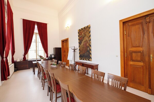 A dining area with a long wooden table, red curtains, and a large painting on the wall. - Klášter Želiv  (Želiv)