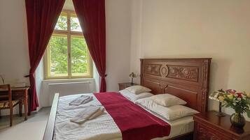 Un dormitorio con cama de madera, cortinas rojas, un escritorio y una ventana con vistas a zonas verdes.