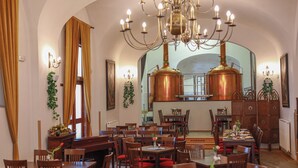 Ein Restaurant mit mehreren Tischen und Stühlen, einer Kandelaber und Kupfergeschirr an der Wand.