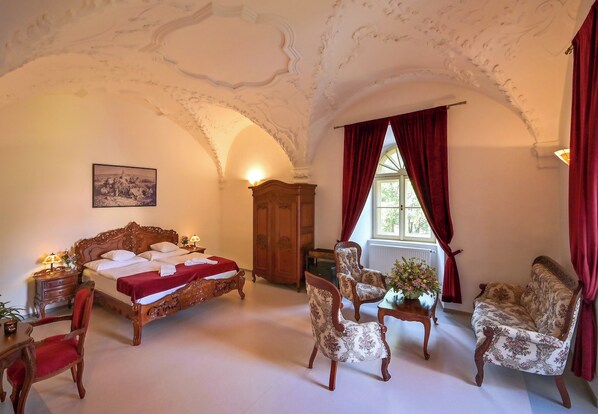 A room with a large bed, two armchairs, a wooden cabinet, and a window with red curtains. - Klášter Želiv (Želiv)