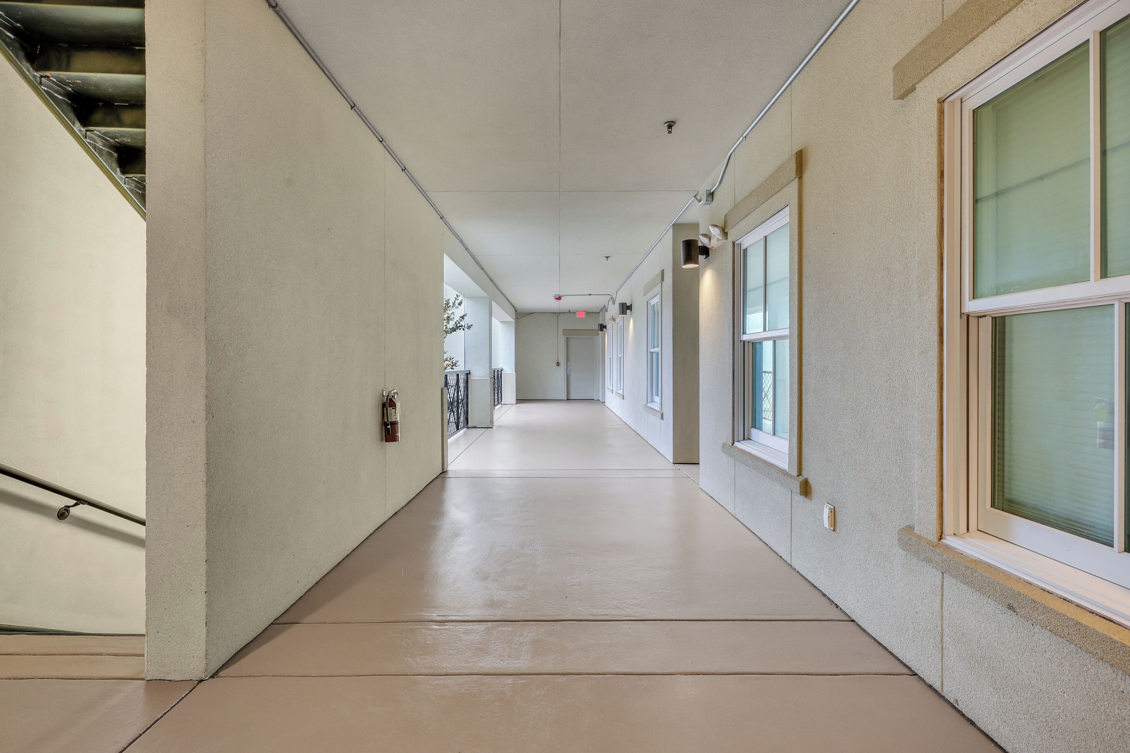 A long, narrow hallway with a tiled floor, white walls, and large windows on one side.
