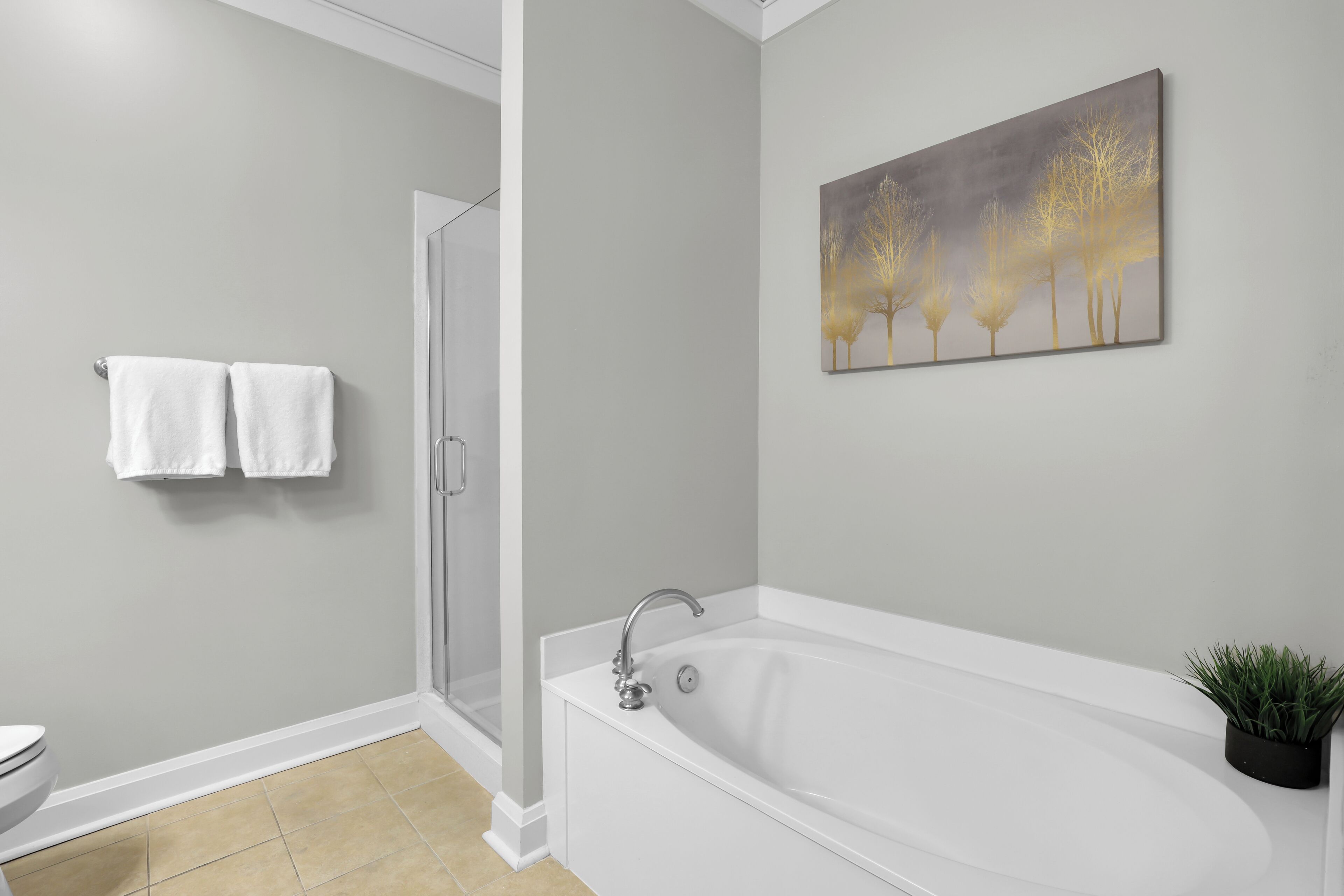 A modern bathroom with a bathtub, a shower, and a toilet. There are two white towels hanging on the wall.