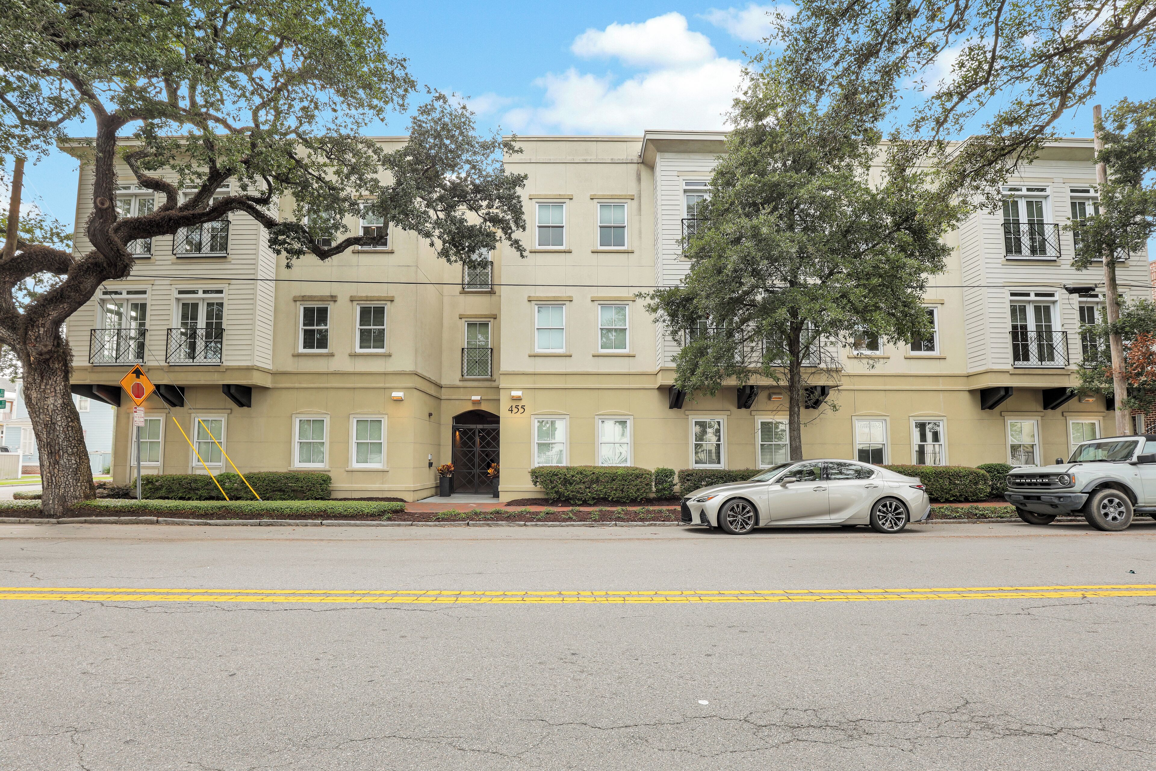 A multi-story residential building with a beige facade, large windows, and a tree in front.