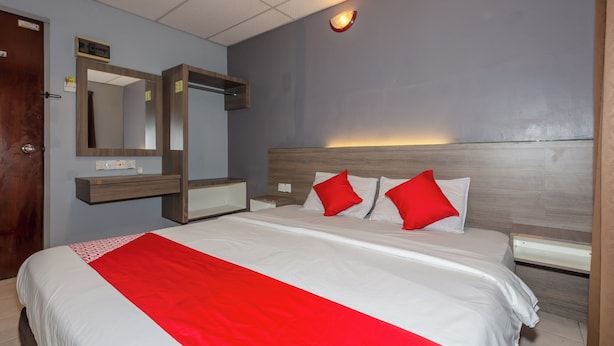 A hotel room with a large bed, a wooden headboard, a bedside table, a mirror, and a red accent wall. - OYO 91258 Qish Hotel Banda Kaba (Malacca City)