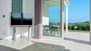 Una sala de estar moderna con un televisor de pantalla plana, un sofá y un ventanal corredero que da a un patio exterior con una mesa y sillas.