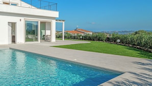 Una casa moderna con piscina, un patio cubierto y vistas al mar.
