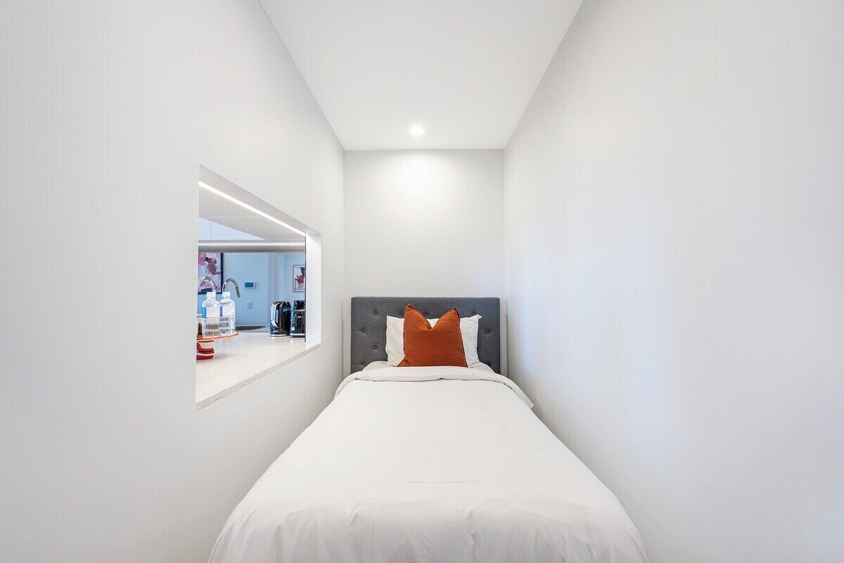 Ein modernes Schlafzimmer mit einem Einzelbett, einer grauen Kopfteil und einer weißen Wand.