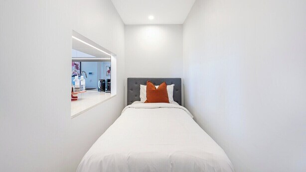 Ein modernes Schlafzimmer mit einem Einzelbett, einer grauen Kopfteil und einer weißen Wand.