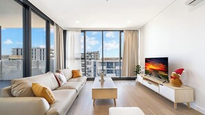 Ein modernes Wohnzimmer mit Sofa, Couchtisch, Fernseher und einem großen Fenster mit Blick auf die Stadt.