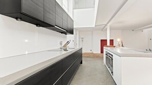 A modern kitchen with a long countertop, dark cabinets, and a built-in oven. - Architect design maisonette in top location in Holland Park (London)
