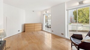 A spacious room with a wooden floor, a bench, and a large window offering a view of the street. - Architect design maisonette in top location in Holland Park (London)