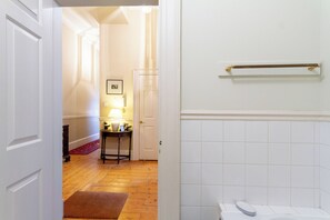 Ein Flur mit Holzboden, einer weißen Tür, einem kleinen Tisch mit einer Lampe und einer weißen Fliesenwand.