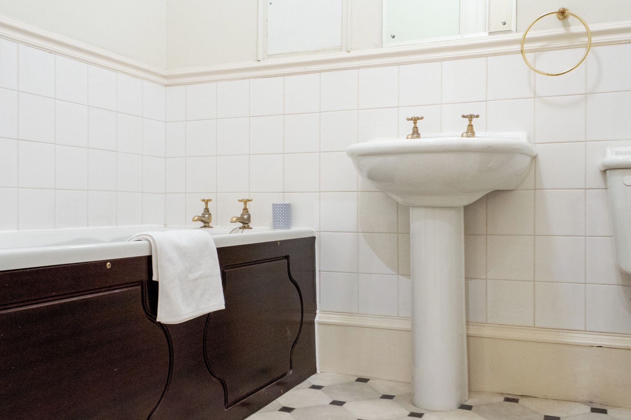 A bathroom with a dark wooden vanity, a white pedestal sink, and a gold faucet.