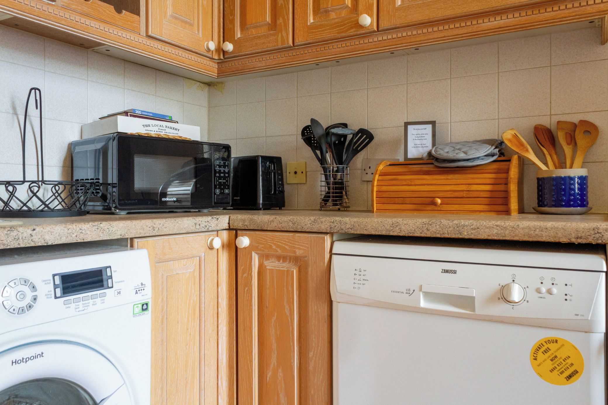 A kitchen with a microwave, toaster, and dishwasher. There are wooden cabinets and a tiled backsplash.