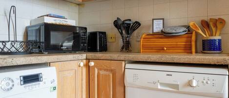 A kitchen with a microwave, toaster, and dishwasher. There are wooden cabinets and a tiled backsplash.