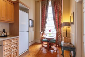 A kitchen with wooden cabinets, a refrigerator, a dining table with chairs, and a window with curtains. - Classic 2 BDR Georgian Flat in Central Edinburgh (Edinburgh)