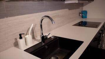 Una cocina moderna con un lavamanos negro, encimera blanca y una cafetera azul.