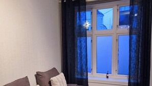Une chambre à coucher avec un grand lit, des rideaux sombres et une fenêtre donnant sur des immeubles.