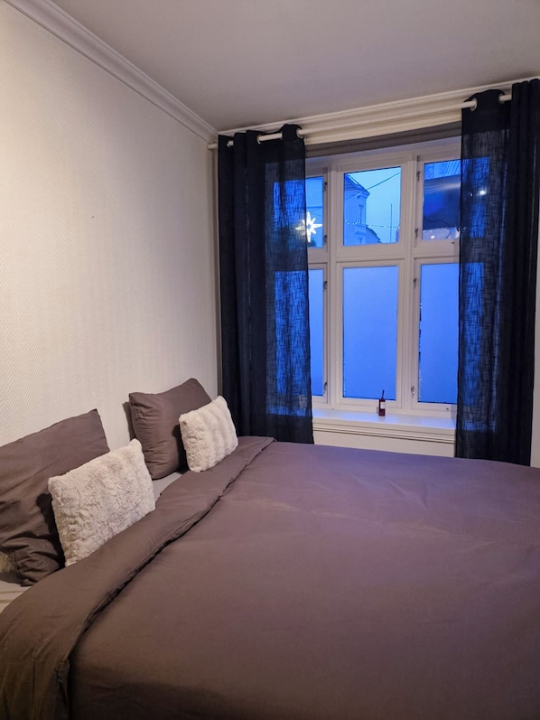 Ein Schlafzimmer mit einem großen Bett, dunklen Vorhängen und einem Fenster mit Blick auf Gebäude.