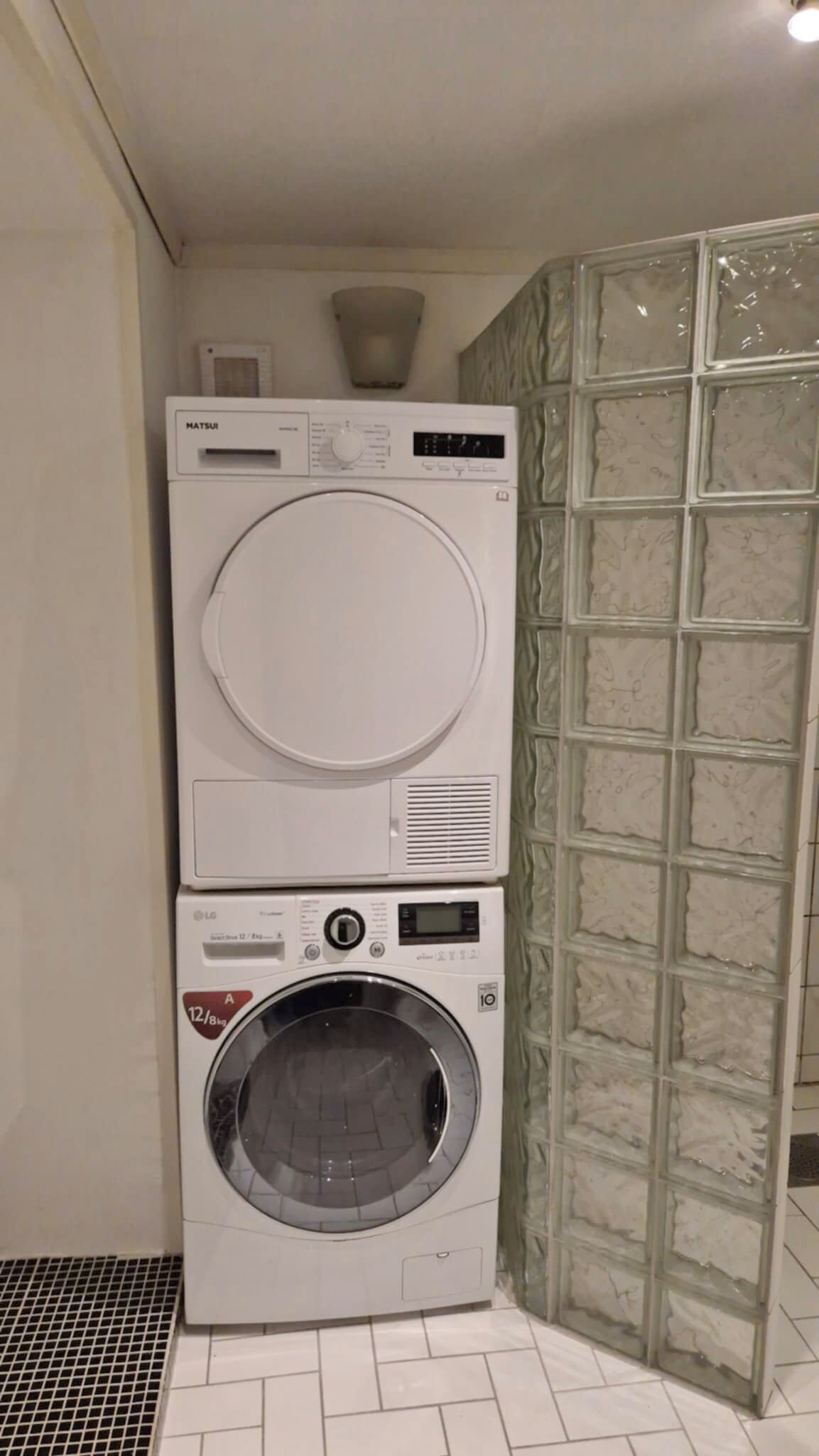 Un appareil combiné lave-linge et sèche-linge, installé dans un coin, avec un sol carrelé et un mur à texture.