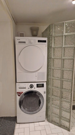 Eine gestapelte Waschmaschine und ein Trockner in einer Ecke, mit Fliesenboden und einer strukturierten Wand.
