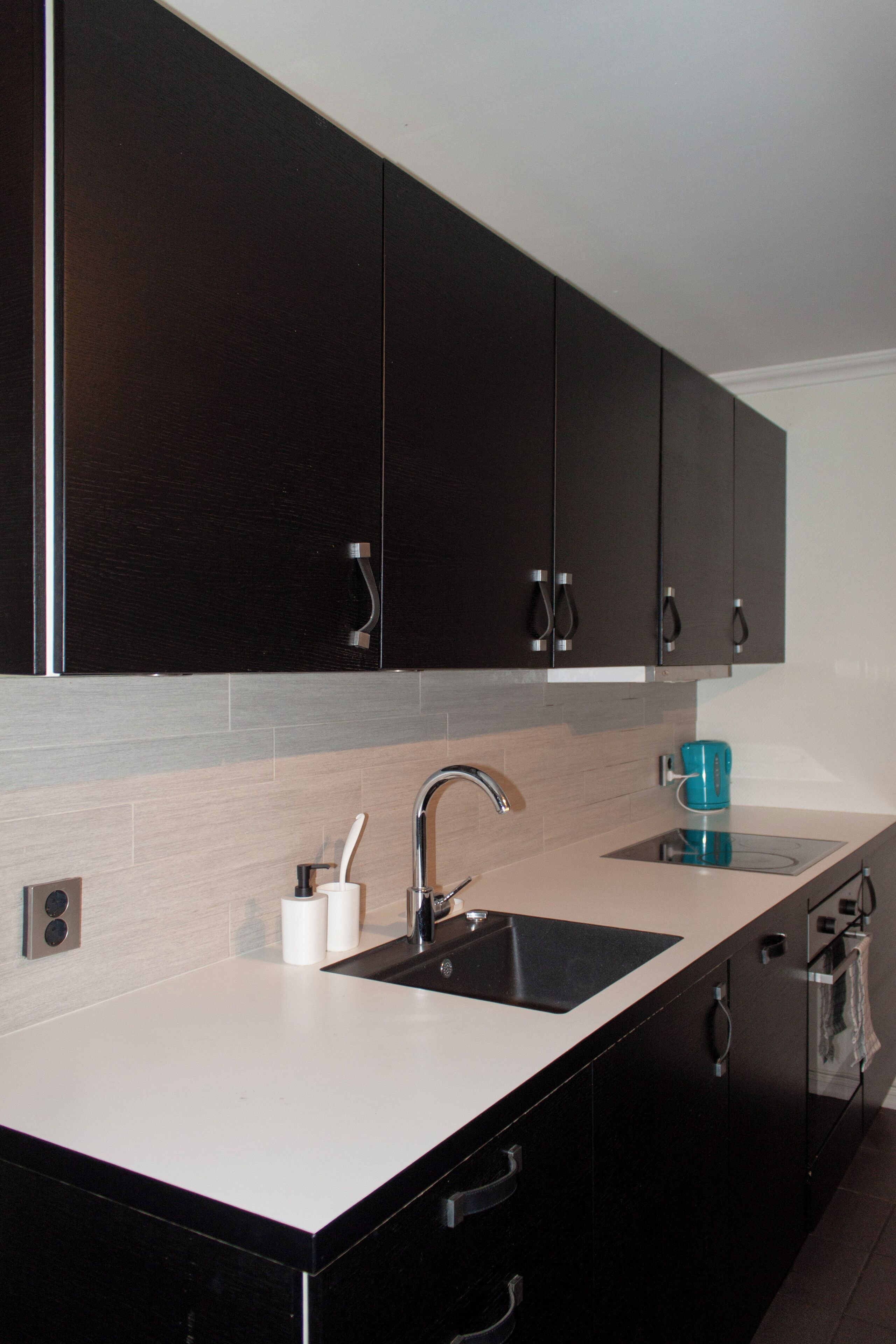 A modern kitchen with dark cabinets, a white countertop, a sink, and a coffee maker.