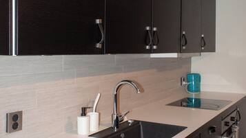 A modern kitchen with dark cabinets, a white countertop, a sink, and a coffee maker.